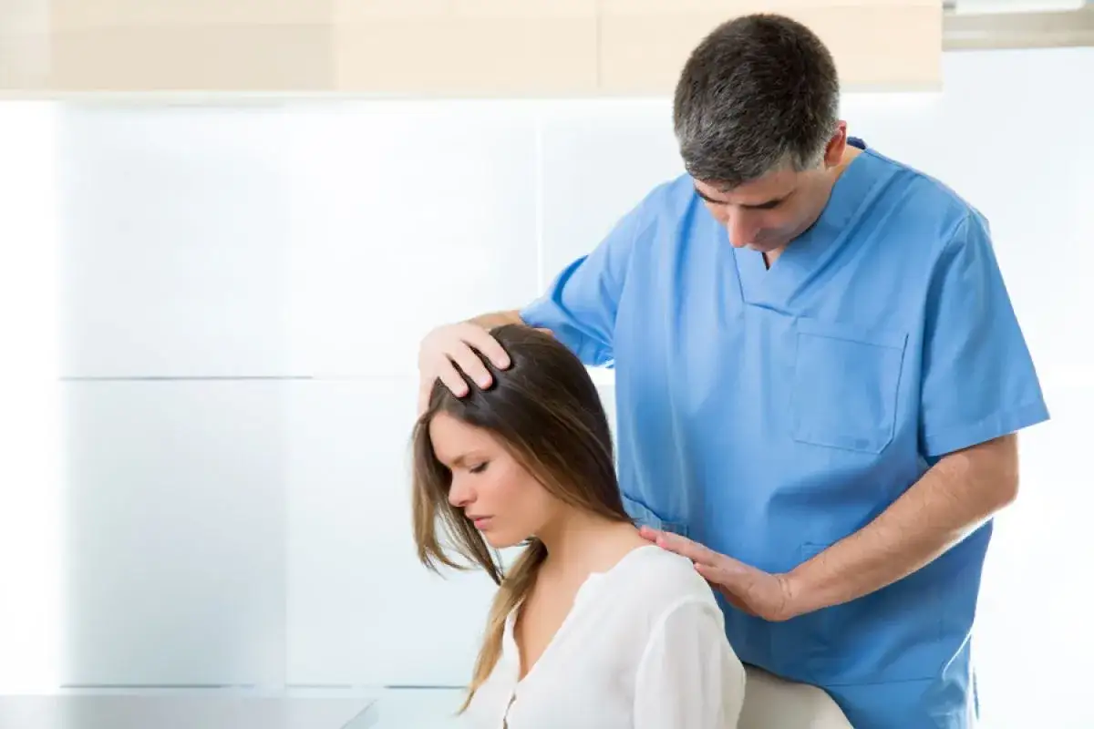 Médico examina a mujer con posible miastenia gravis. Sus manos tocan su cabeza y hombros.