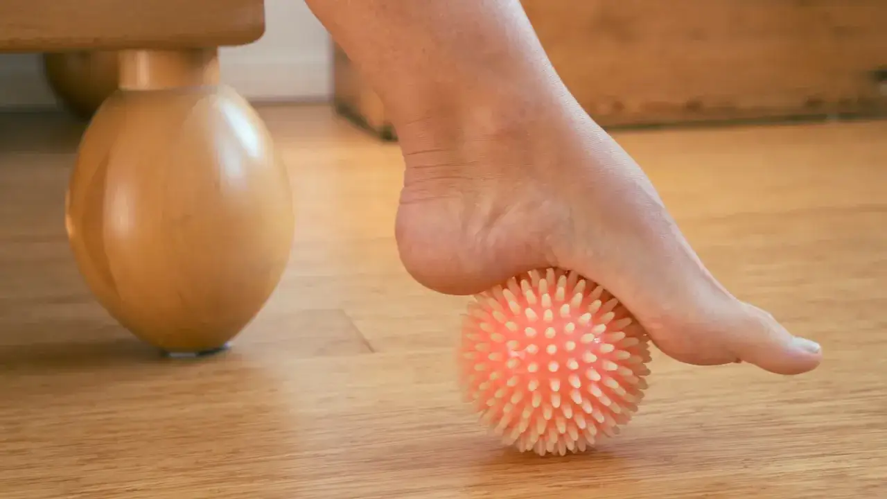 Pie rodando sobre una pelota con púas para aliviar la neuropatía periférica.