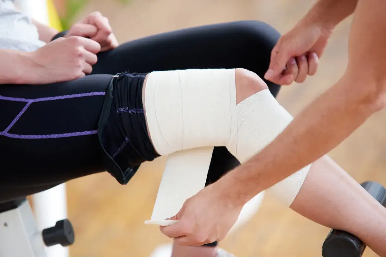 Aplicación del método RICE para tratar una lesión de rodilla, vendando la zona afectada para reducir la inflamación y el dolor.