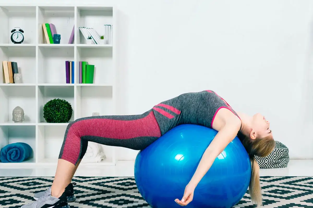 Mujer estirando la espalda en pelota azul, aliviando una contractura lumbar.