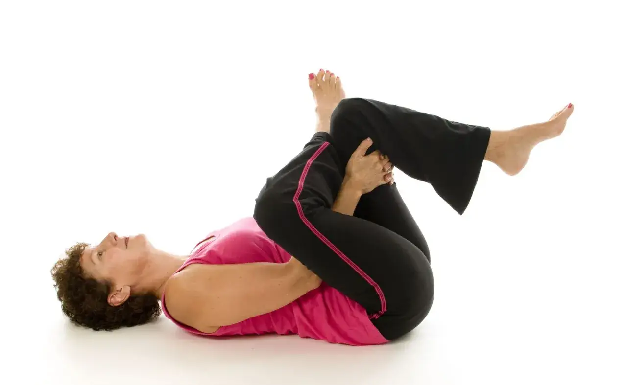 Mujer haciendo estiramiento de rodilla al pecho, &uacute;til para aliviar el s&iacute;ndrome piriforme.