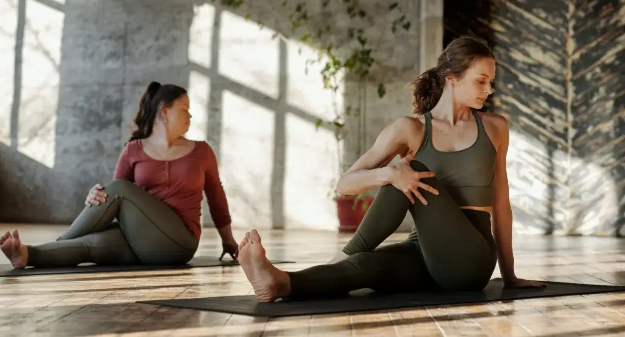 Dos mujeres realizan una torsión sentada, un ejercicio ideal para aprender cómo estirar la espalda baja y mejorar la flexibilidad.